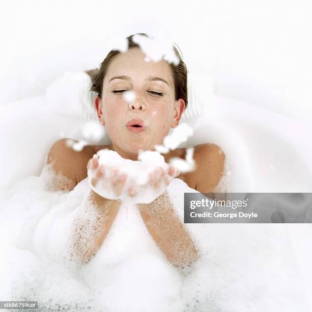 portrait of a young woman in a bathtub blowing foam from her hands - her fotografías e imágenes de stock