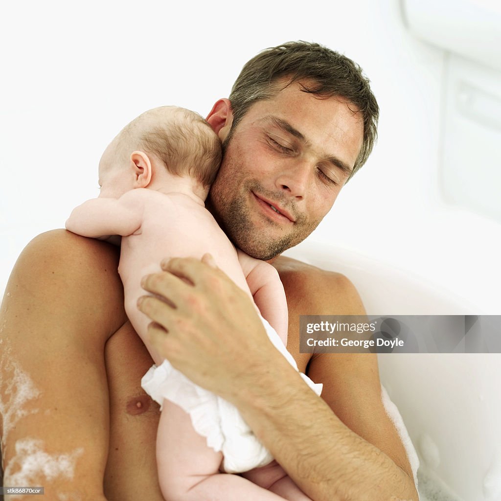 Father holding his baby daughter (6-12 months) in a bathtub