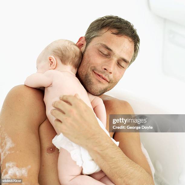 father holding his baby daughter (6-12 months) in a bathtub - genderblend stock pictures, royalty-free photos & images