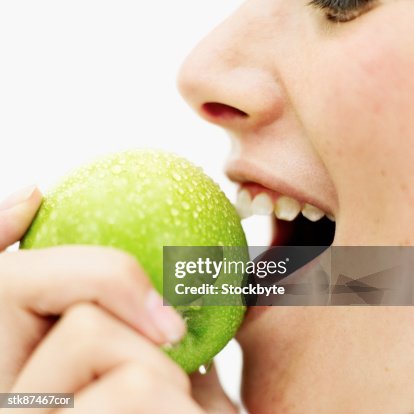 Side view of a teenage girl (15-16) biting into a green apple Side view of a teenage girl (15-16) biting into a green apple