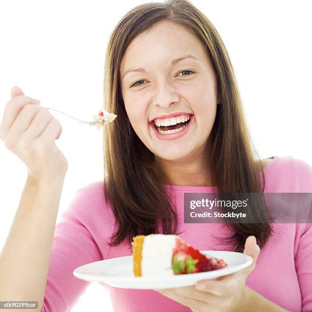 portrait of a young woman holding a fork in one hand and a plate with a slice of cake in the other - slice stock pictures, royalty-free photos & images
