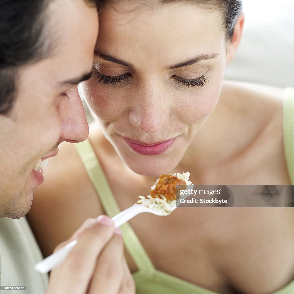 Close-up of a young man feeding a young woman with a plastic fork