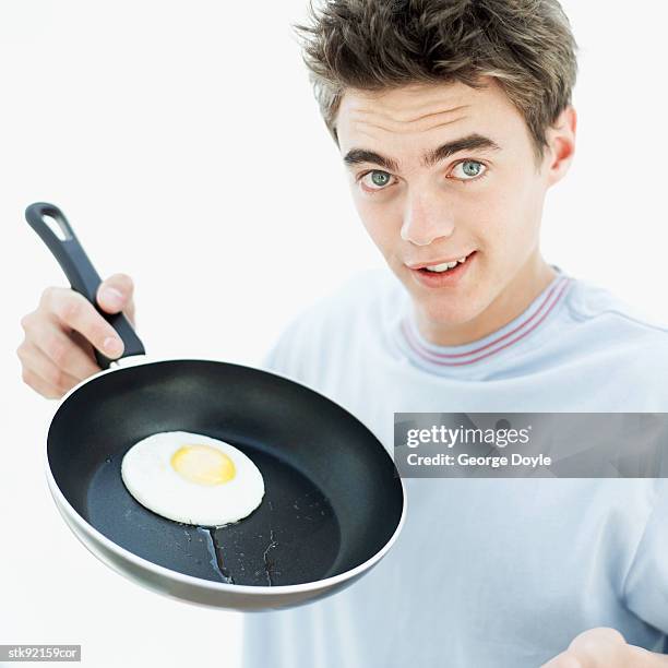 teenage boy (16-17) with a fried egg in a frying pan - pan stock-fotos und bilder