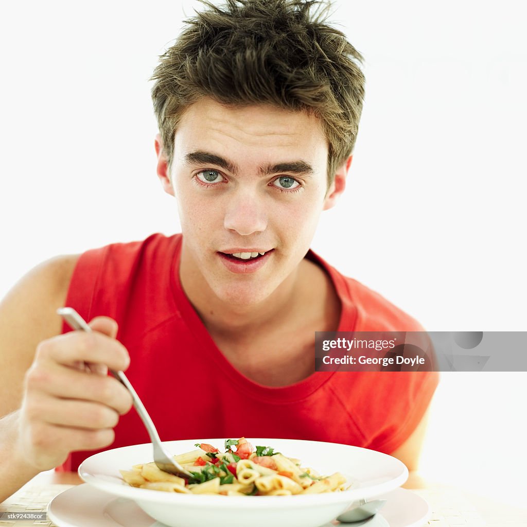 Teenage boy (16-17) eating pasta from a bowl