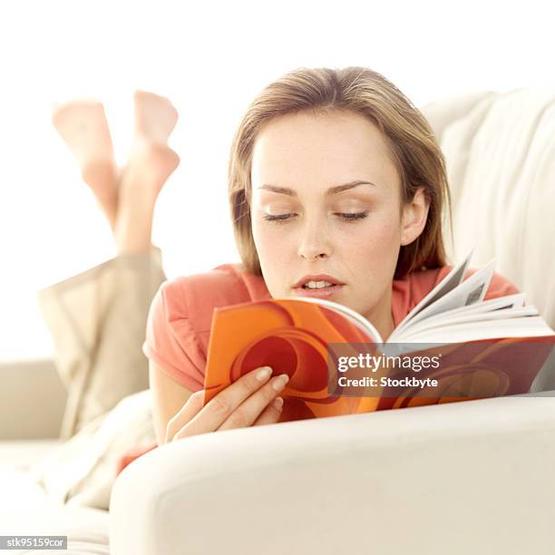 portrait of a young woman lying on a couch reading - libro en rústica fotografías e imágenes de stock