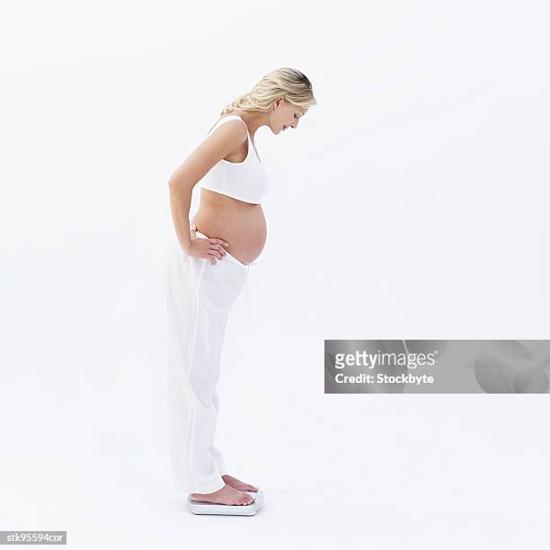 side view of a pregnant woman standing on a weighing scale - alleen mid volwassen vrouwen stockfoto's en -beelden