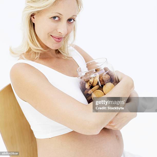 pregnant woman holding a jar of biscuits against her chest - her fotografías e imágenes de stock