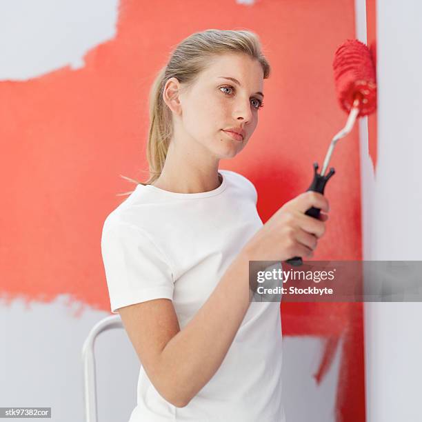 side view of a woman painting a wall red with a roller - roller fotografías e imágenes de stock