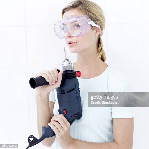 young woman with a power drill blowing on the drill bit - bit stock-fotos und bilder