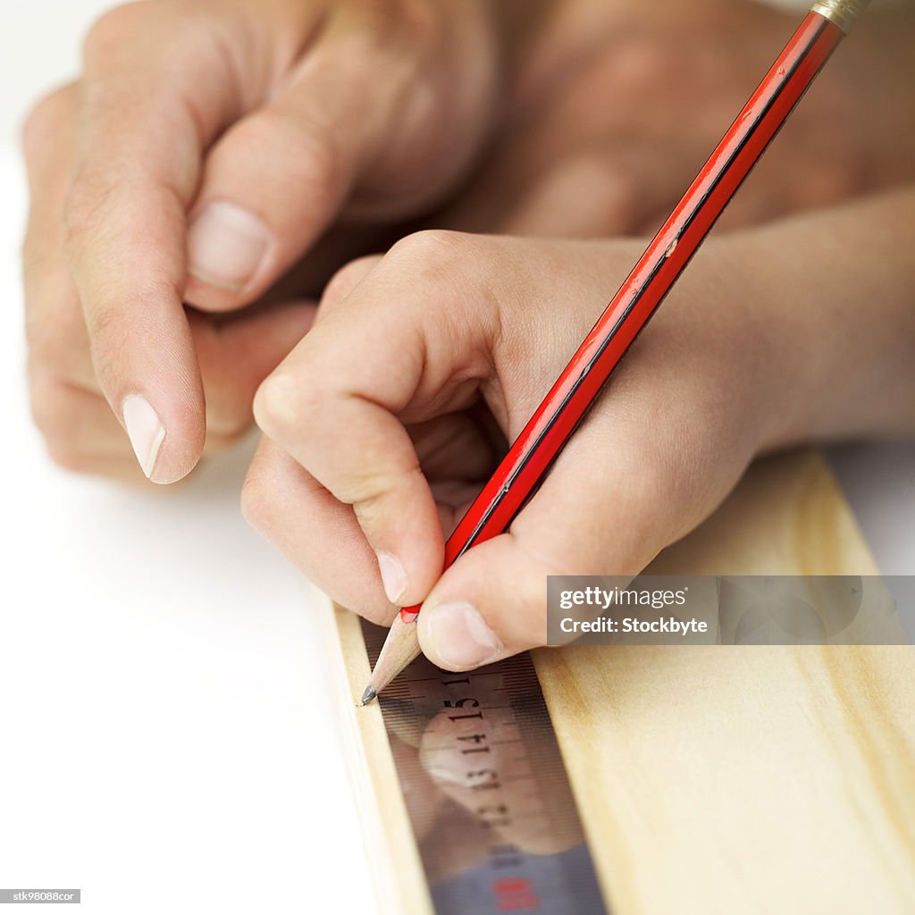 Close-up of a person drawing a line with a pencil and a metal scale