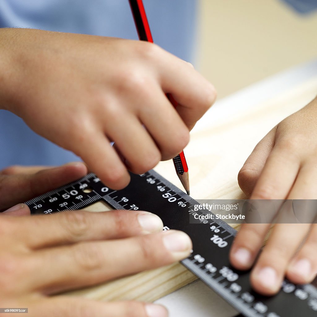 Close-up of a person drawing a line with a pencil and right angle scale