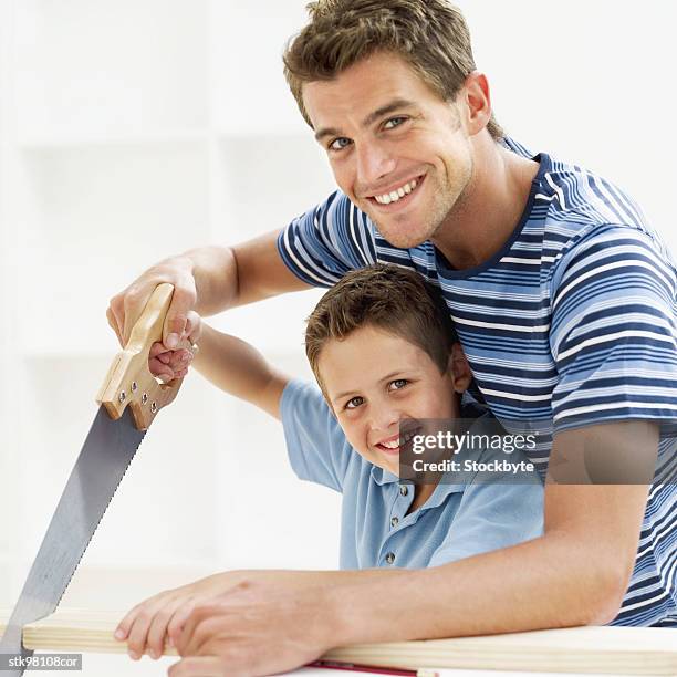 close-up of a man helping his son saw a piece of wood - radius with the cinema society brooks brothers host the new york premiere of adult beginners stockfoto's en -beelden