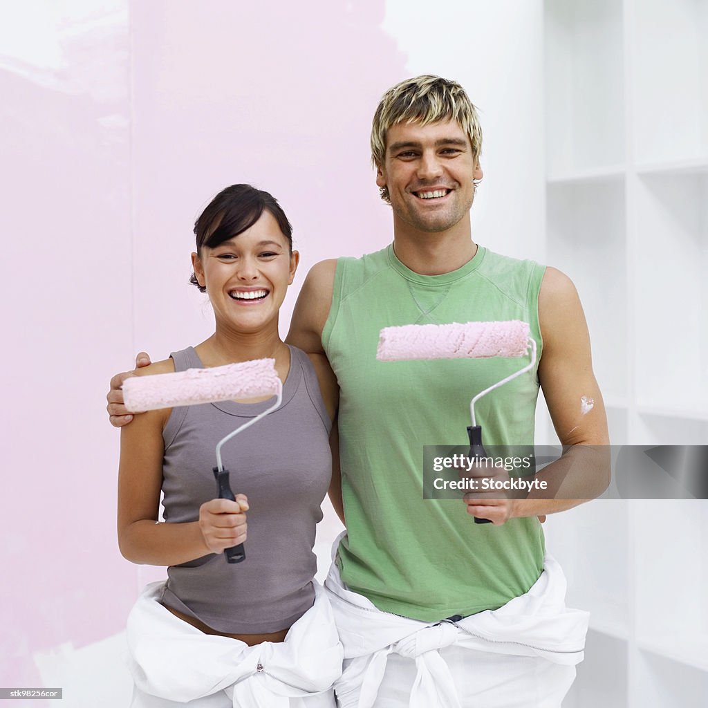 Portrait of a couple holding paint rollers dipped in pink paint