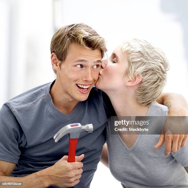 portrait of a young man with a hammer being kissed on the check by a young woman - check up ストックフォトと画像