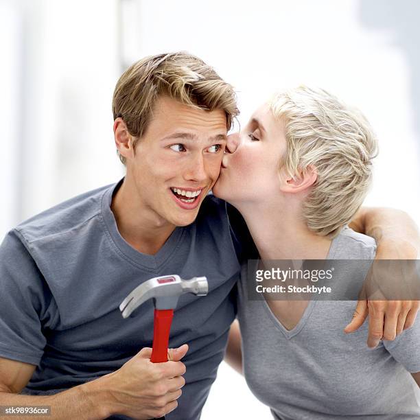 portrait of a young man with a hammer being kissed on the check by a young woman - by stock pictures, royalty-free photos & images