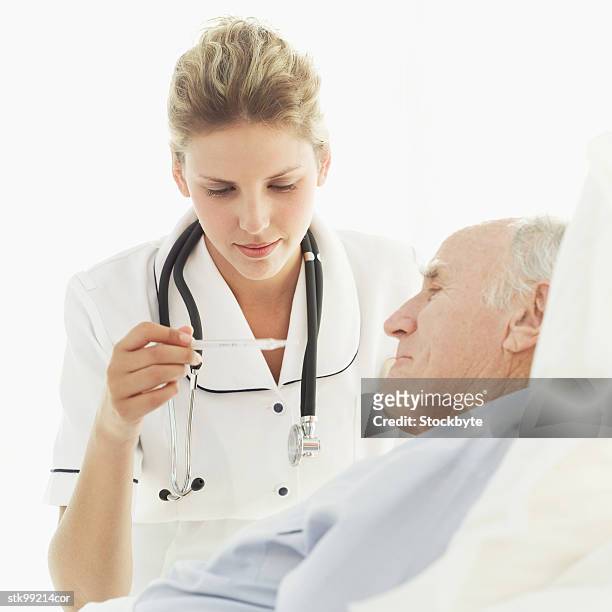 female nurse reading a thermometer sitting next to an old man - next stockfoto's en -beelden