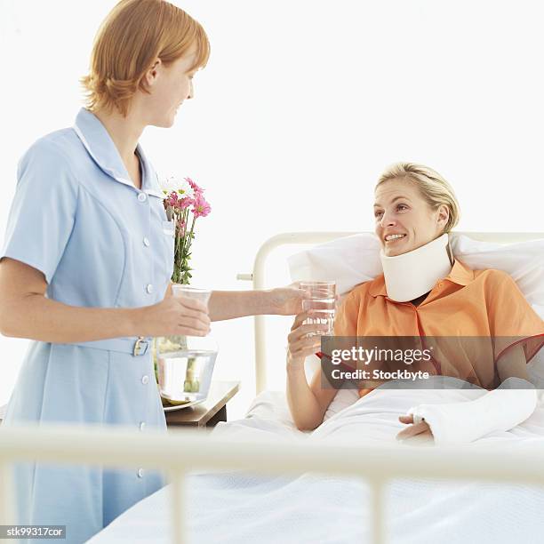 female nurse giving a glass of water to a woman wearing a neck brace and an arm cast - wearing stock-fotos und bilder