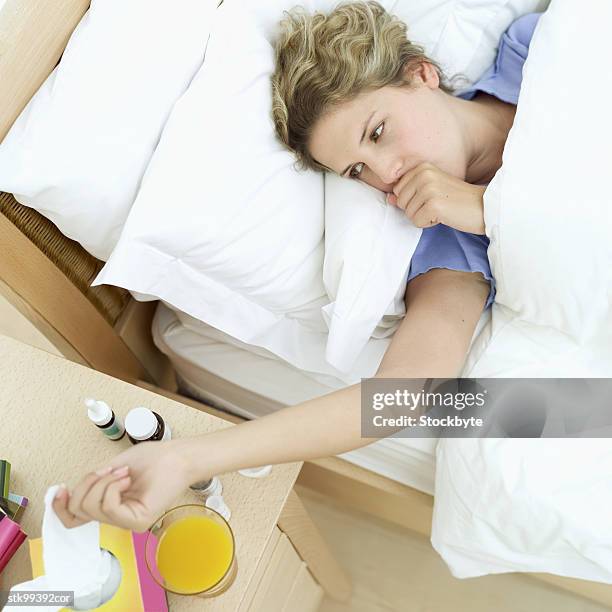 woman lying in a bed reaching for a tissue on the bed side table - human limb stock pictures, royalty-free photos & images