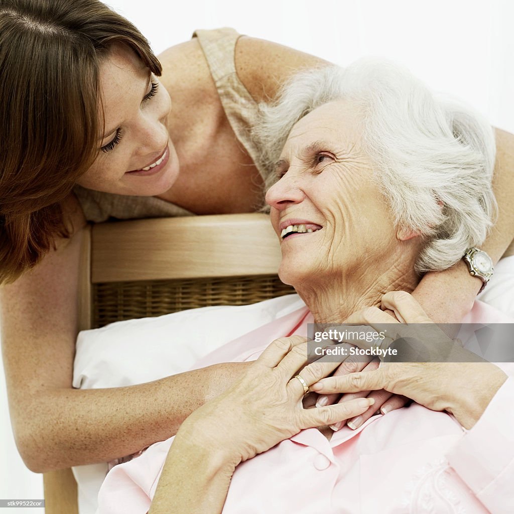 Woman smiling and holding an old woman in bed