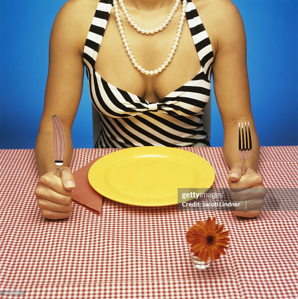 Woman sitting at table with empty plate, holding cutlery