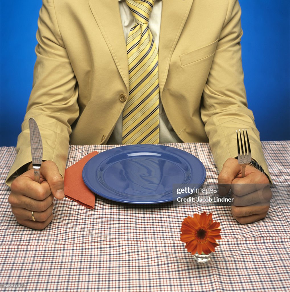 Man sitting at table with empty plate, holding cutlery