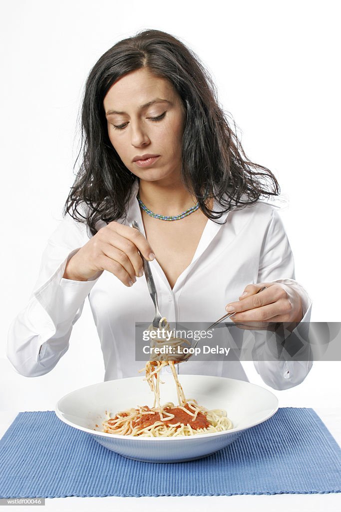 Young woman eating bowl of spaghetti with fork, portrait