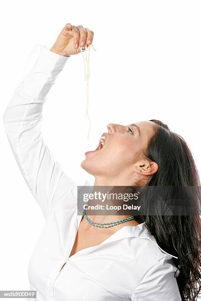 young woman holding noodles in hand above mouth - miembro humano fotografías e imágenes de stock