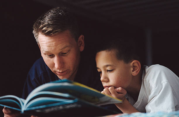 a father reads a book to his son laying on the bed