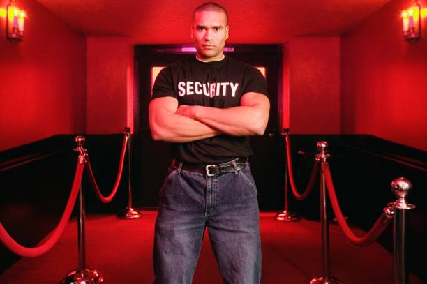 african male bouncer with arms crossed next to velvet ropes picture