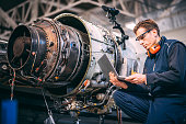 Aircraft engineer in a hangar using a laptop while repairing and maintaining an airplane jet engine