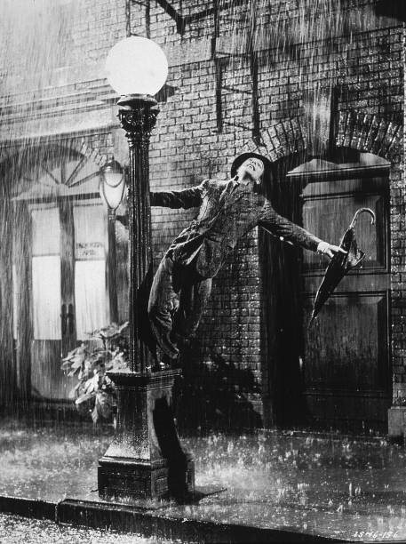 American actor and dancer Gene Kelly swings from a lamp post in a still from the film, `Singin` In The Rain` directed by Kelly and Stanley Donen,...