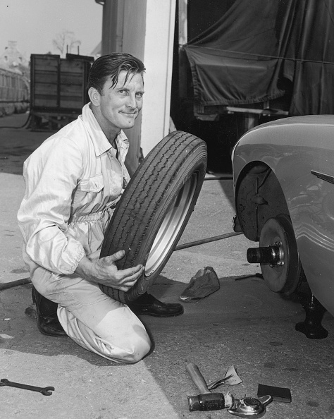 american-actor-kirk-douglas-kneels-to-change-a-tire-on-his-during-a-picture-id3172576