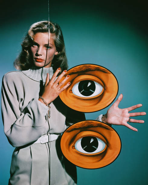 American actress Lauren Bacall poses behind a pane of glass decorated with two giant eyes, circa 1950.