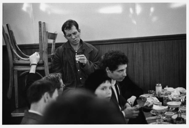 American Beat writer Jack Kerouac holds a cup of tea as he stands near a crowded table at a Chinese restaurant, New York, New York, 1959.