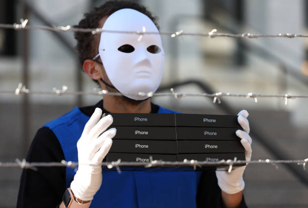 An activist with the group SumOfUs holds a stack of iPhone boxes as he wears a costume depicting Uyghurs in a mock forced labor camp as he stages a...