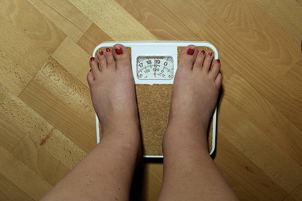 An anonymous woman on the scales before her weight loss surgery. The scales stop at 19 stone, but she weighs nearly 20 stone and is severely obese....