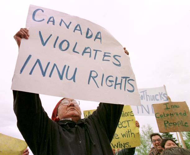 As Queen Elizabeth II's motorcade drives by, an Innu woman holds up a sign protesting Canada's claim to their lands in Sheshatshiu, Newfoundland...