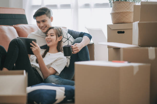 asia chinese couple sitting on floor resting after opening carton cardboard boxes in living room moving house - couple stock pictures, royalty-free photos & images