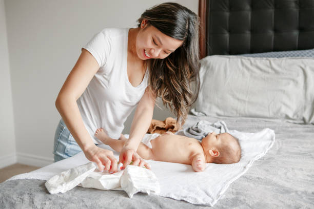 asian busy mother changing diaper clothes for newborn baby son at home - dealing with diapers stock pictures, royalty-free photos & images