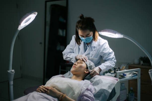 cosmetóloga chinesa asiática usando boné de cabelo protetor descartável para seu cliente em sala de cirurgia - cirurgia plástica - fotografias e filmes do acervo