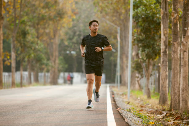 asian sportman jogging and checking smart watch between workout jogging outdoor - exercise stock pictures, royalty-free photos & images