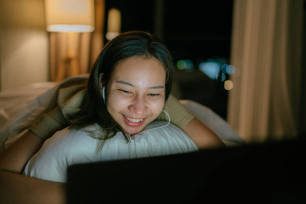 mulher asiática relaxando na sexta à noite em seu apartamento assistindo um filme na tv curtindo uma noite na cama. - streaming - fotografias e filmes do acervo