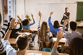 Back view of  high school students raising hands on a class.