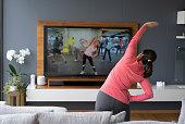 Back view of senior woman following an online stretching class looking at TV screen