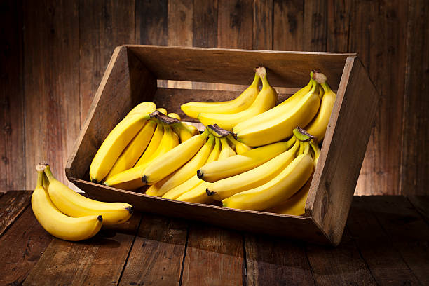 bananas in a crate on rustic wood table - banana stock pictures, royalty-free photos & images