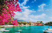 Beautiful Assos village scenery framed with branch of magenta blossom fuchsia flower. Summer vacation concept