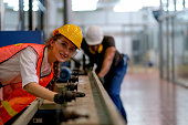 Beautiful worker or technician or engineer woman smile and look forward in front of rail of the machine with her co-worker as background in factory
