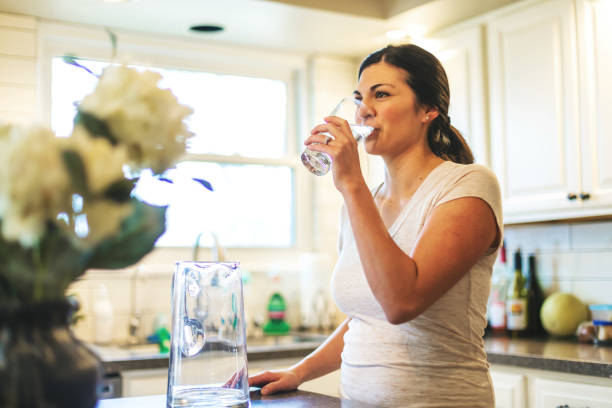 beautiful young adult millennial female using water in residential home - drinking water stock pictures, royalty-free photos & images