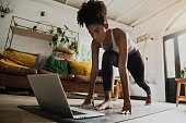 Beautiful young mixed race woman working out from home, online workout on laptop