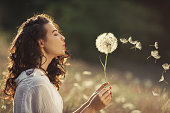 Beautiful Young Woman Blows Dandelion in a Wheat field in the Summer Sunset. Beauty Summer Concept